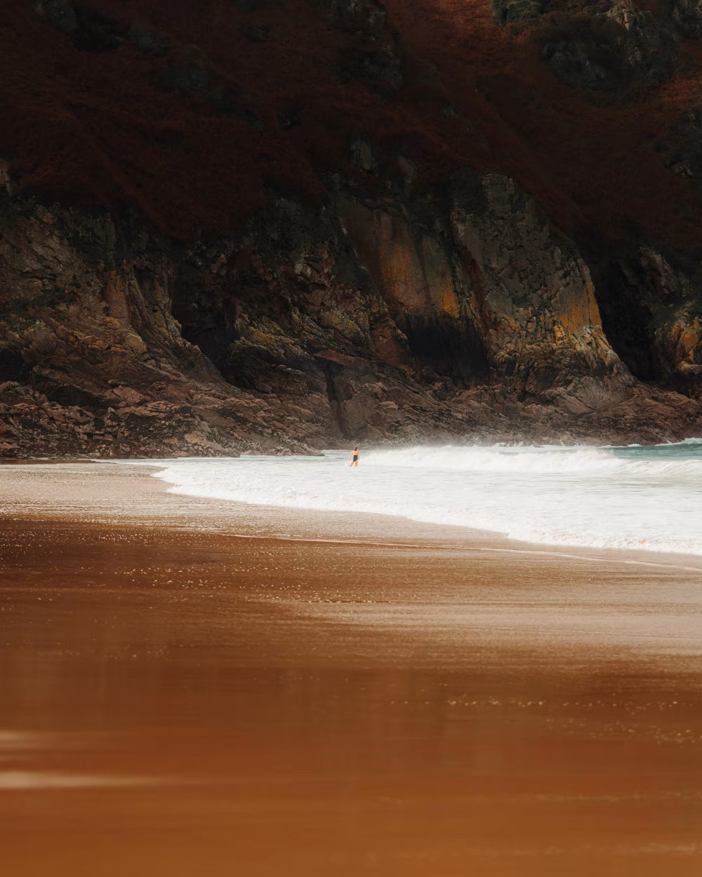 Dramatic Rocky Shoreline with Solitary Person Wading Near Gentle Ocean Waves