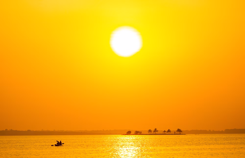 Golden Sunset Over Calm Lake With Silhouetted Canoe and Distant Palm Trees