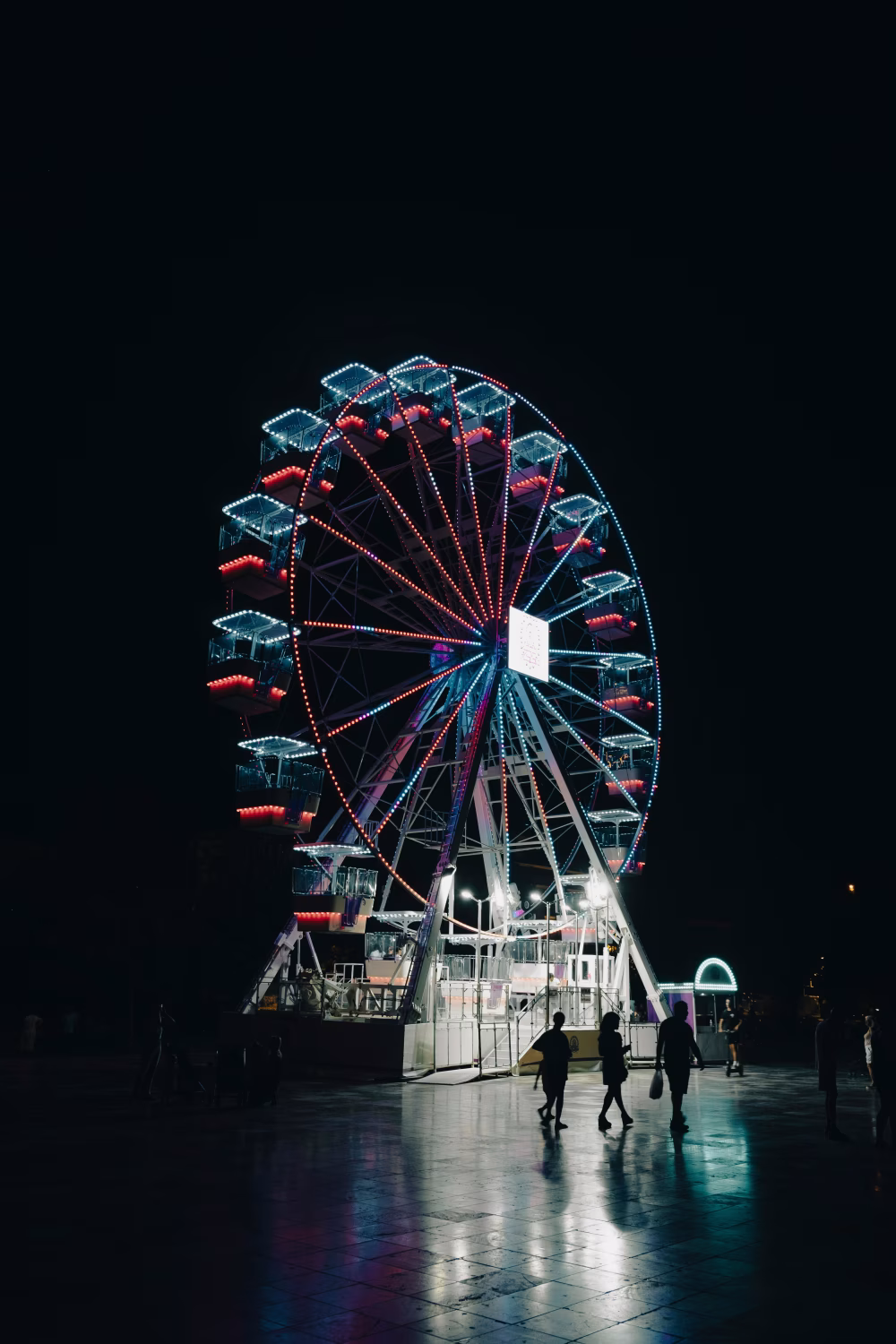 Illuminated Ferris Wheel and Visitors at a Nighttime Fair Landscape