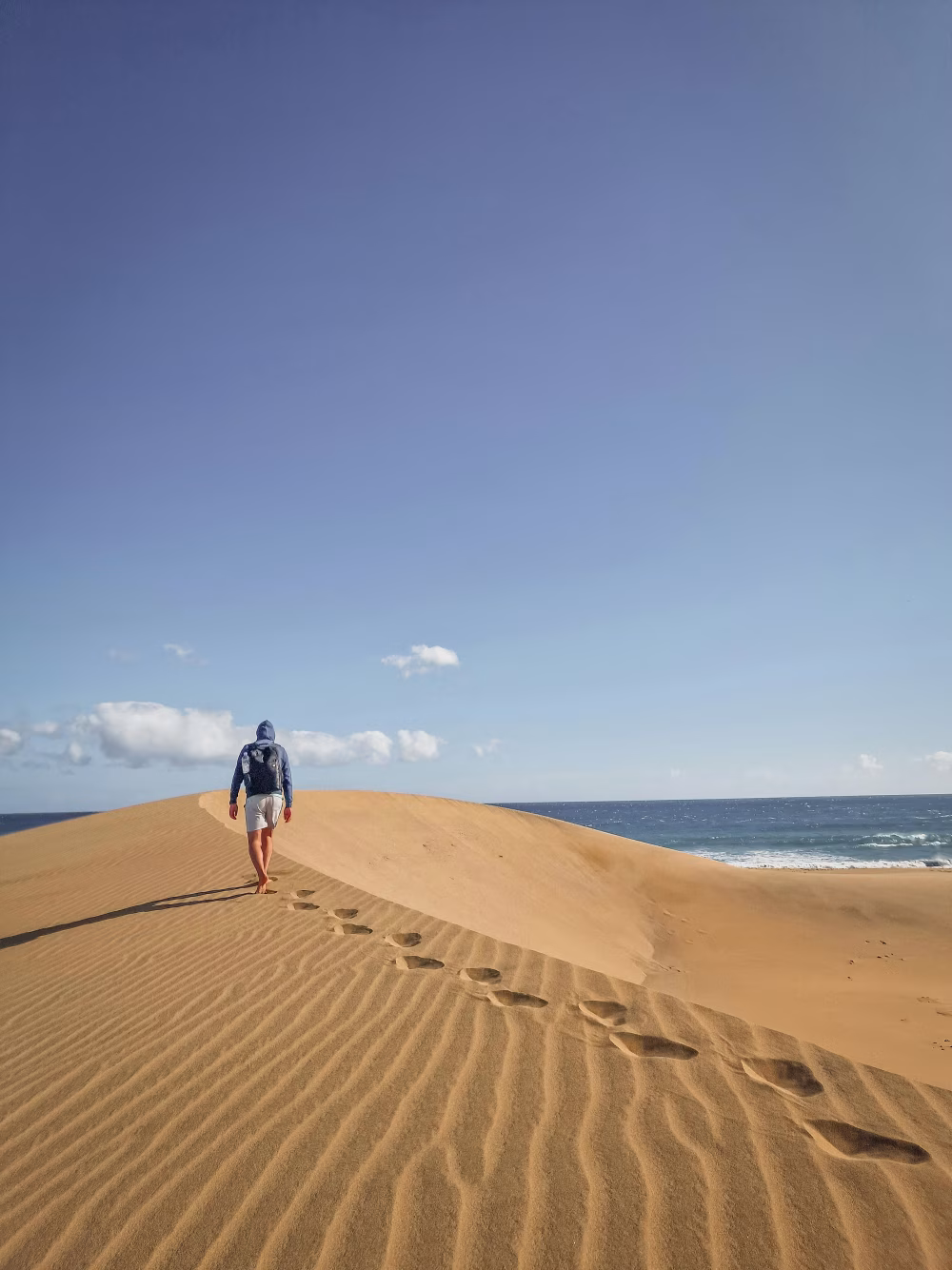 Man Walking on Sandy Beach With Clear Blue Sky and Ocean Views