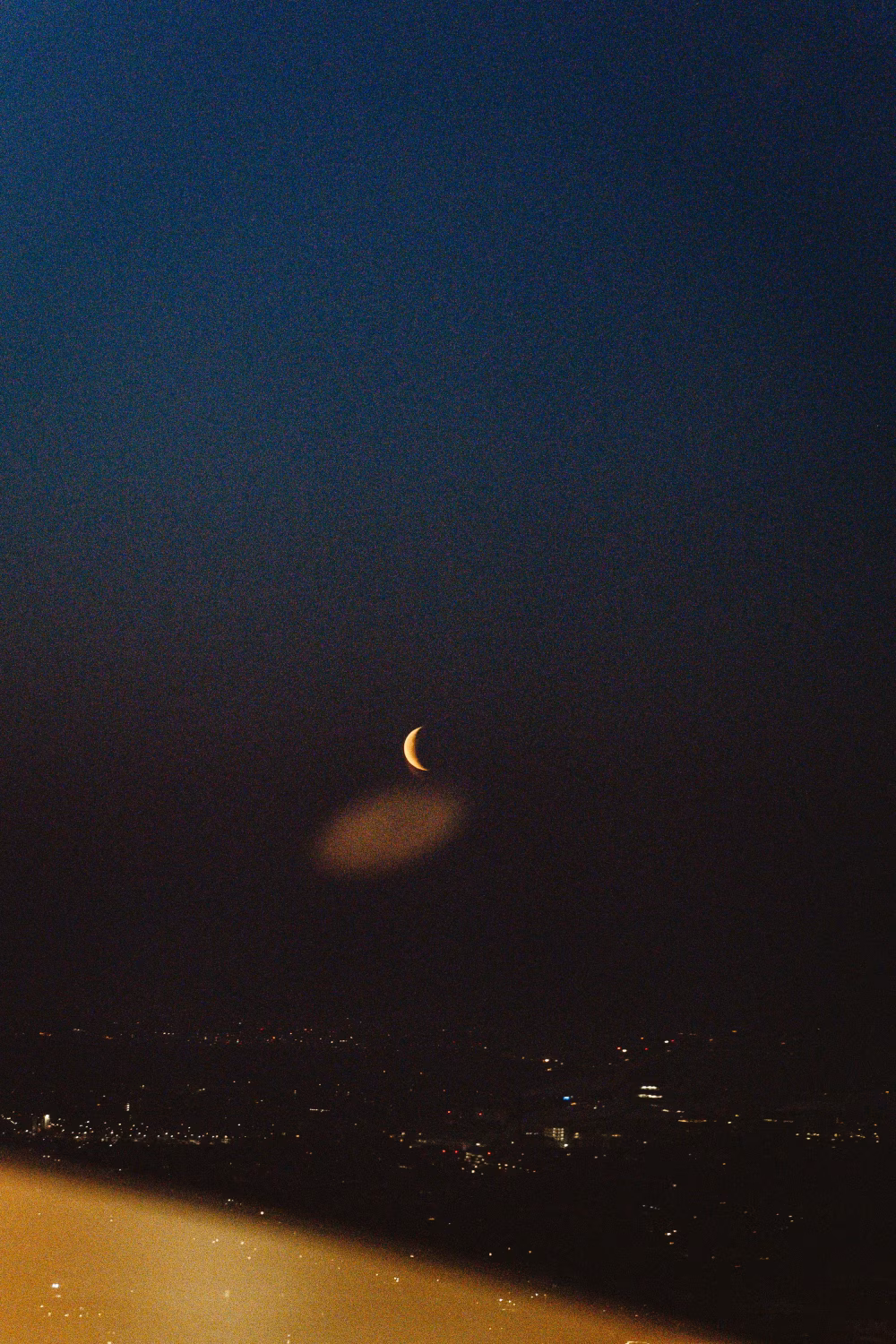 Night Sky with Crescent Moon Above a Cityscape Illuminated by Distant Lights