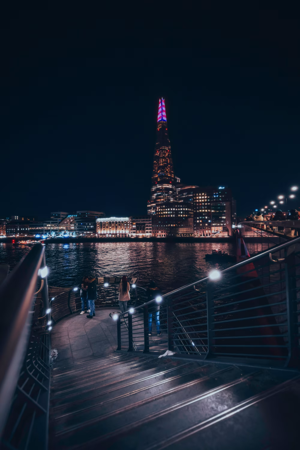 Nighttime Cityscape with Illuminated Skyscraper and Riverfront Pathway