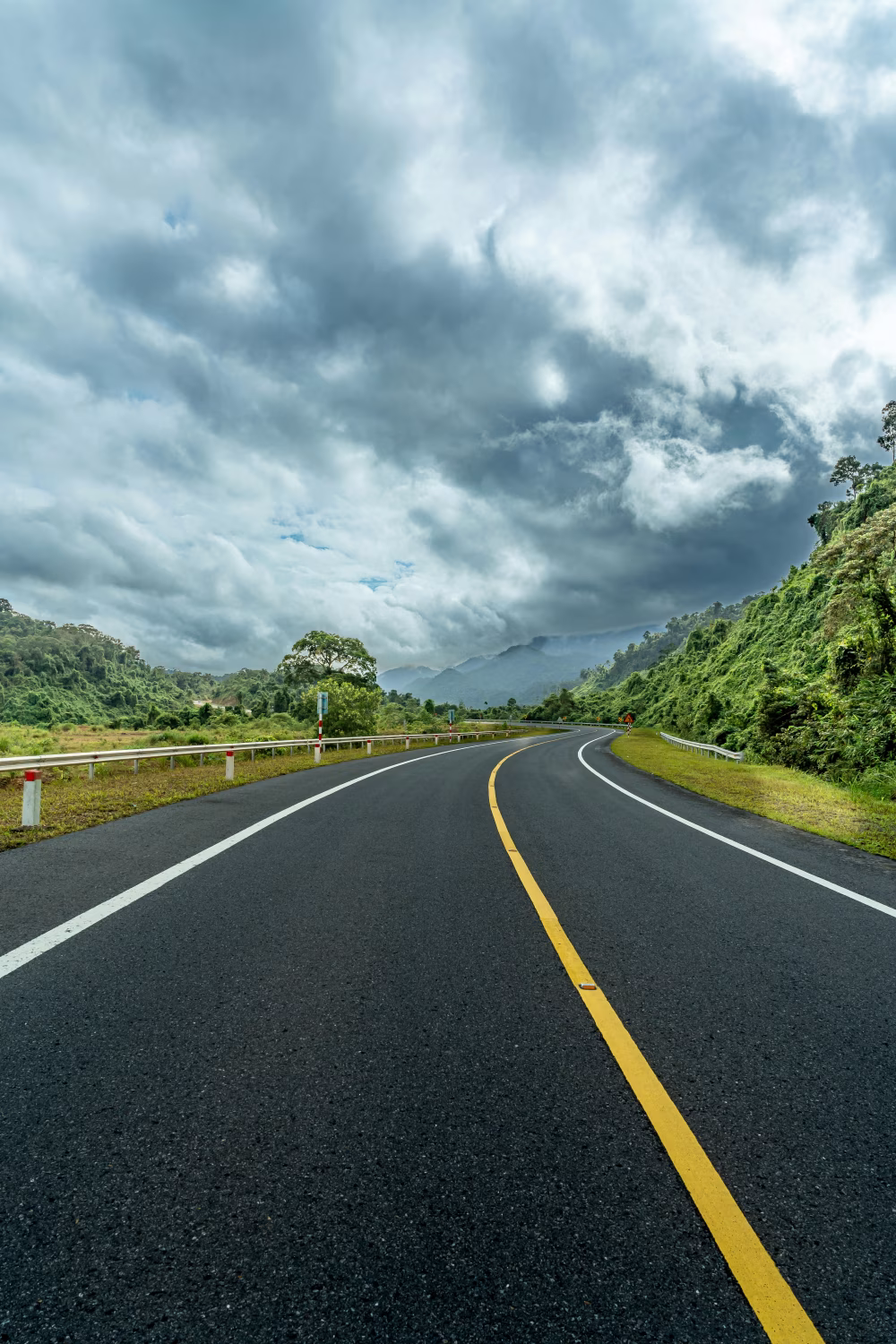 Scenic Curving Road Through Lush Green Hills Under Dramatic Cloudy Sky
