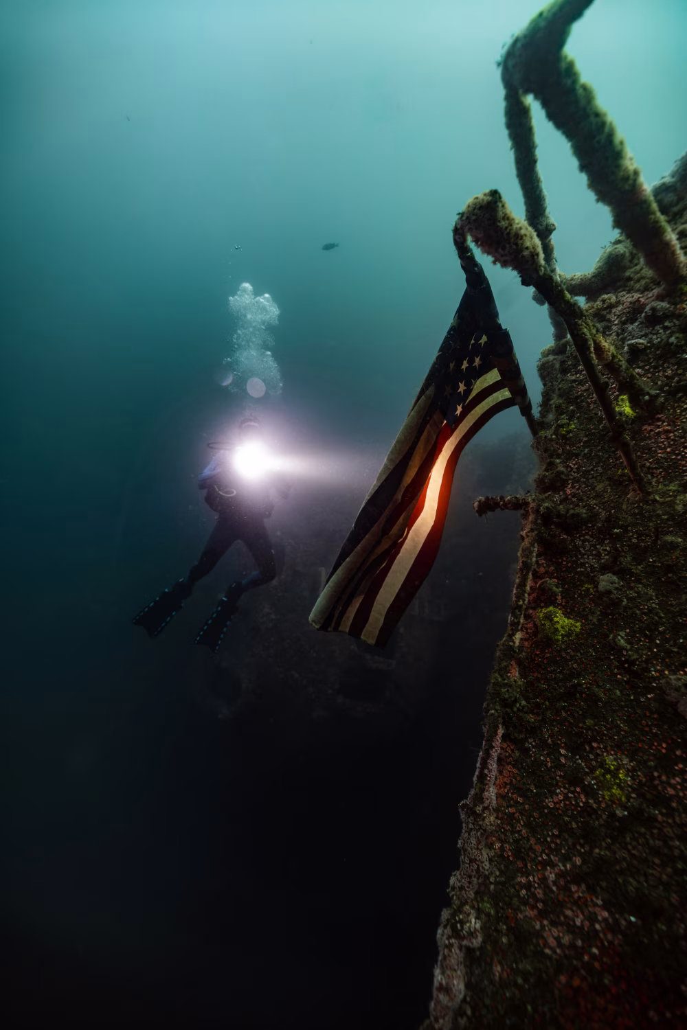 Scuba Diver Exploring Sunken Shipwreck with American Flag Underwater