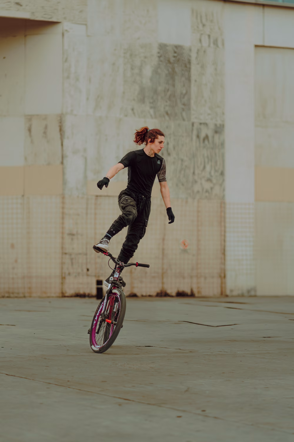 Skilled BMX Rider Performs Balance Trick On Street Near Industrial Concrete Wall