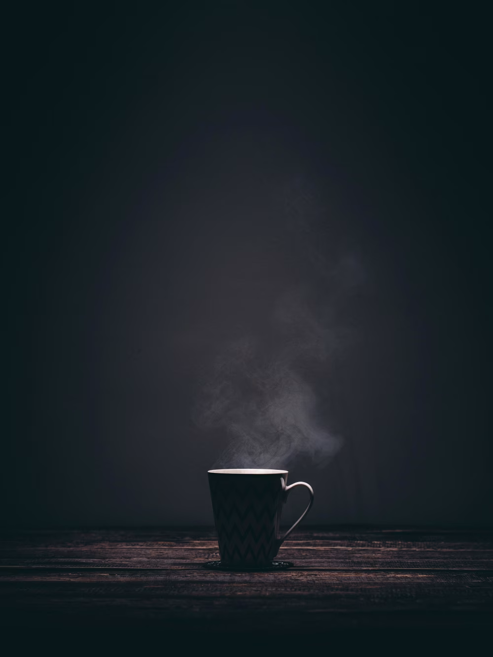 Steaming Cup of Coffee on a Wooden Table in Dim Light Setting