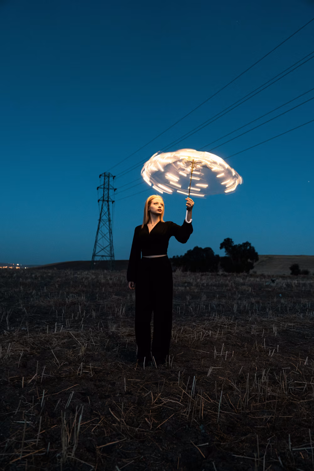 Woman Holding Illuminated Umbrella Outdoors During Twilight in Rural Landscape