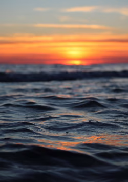 Calm Ocean Waves at Sunset with Vibrant Orange and Yellow Sky