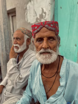 Elderly Men In Traditional Caps Sit Outdoors By Turquoise Wall, Portrait Of Friendship In Urban Setting
