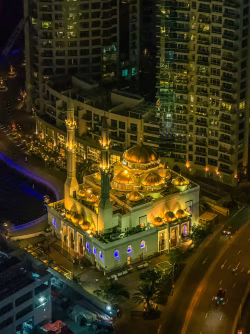 Illuminated Mosque Surrounded by High-Rise Buildings at Night