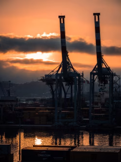 Industrial Port at Sunset With Crane Silhouettes and Cargo Containers by the Water