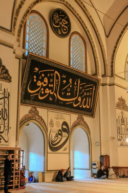 Interior Of Mosque Hall With Large Arabic Calligraphy Panel And Prayer Area
