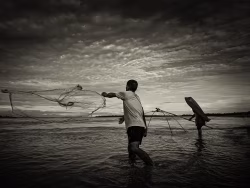 Silhouetted Fishermen Casting Net During Sunset Along Tranquil Riverscape