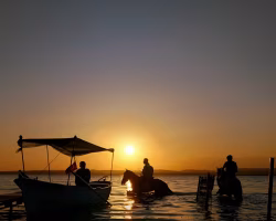 Silhouettes of Riders and Boat Exuding Tranquility Under a Serene Sunset