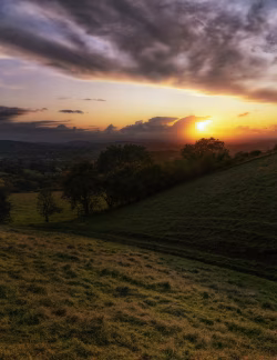 Stunning Sunset Over Serene Rural Landscape with Rolling Hills and Vibrant Clouds