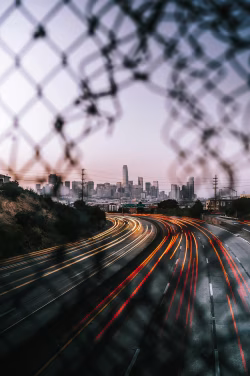 Urban Highway Traffic and City Skyline at Dusk Through Fence