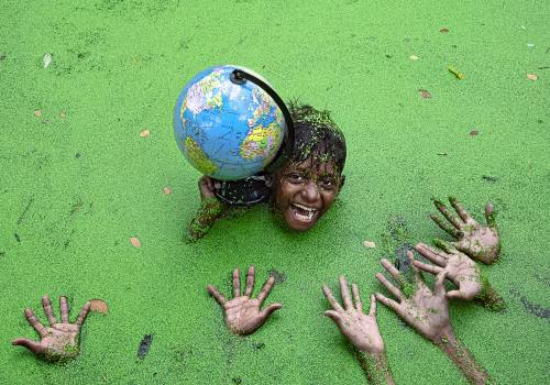 Boy Holding Globe in Vibrant Green Environment with Outstretched Hands