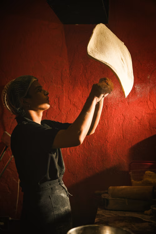 Chef Preparing Pizza Dough in Traditional Kitchen with Red Wall and Dramatic Lighting