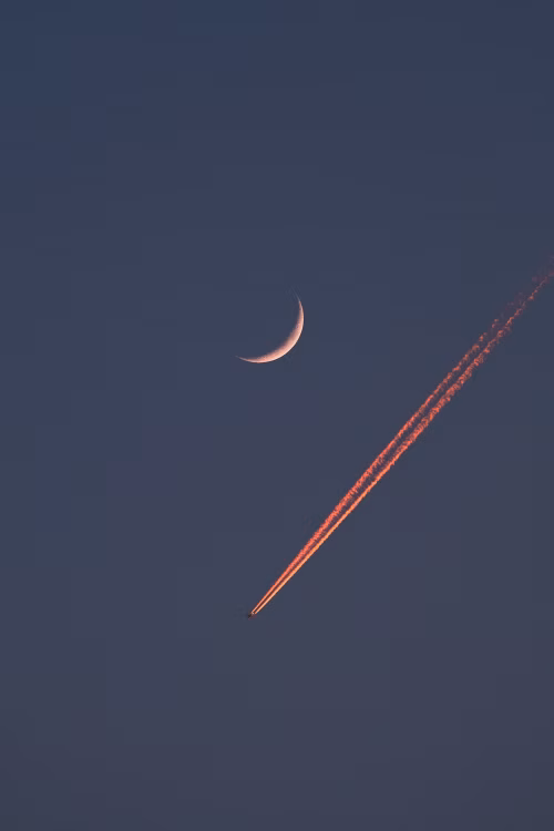 Crescent Moon with Airplane and Vibrant Contrails in Twilight Sky