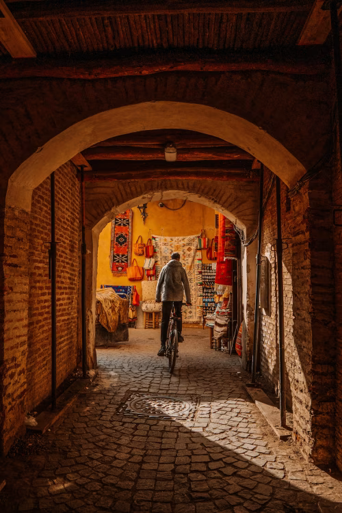 Cyclist Passing Through Brick Archway in a Colorful Market Alley