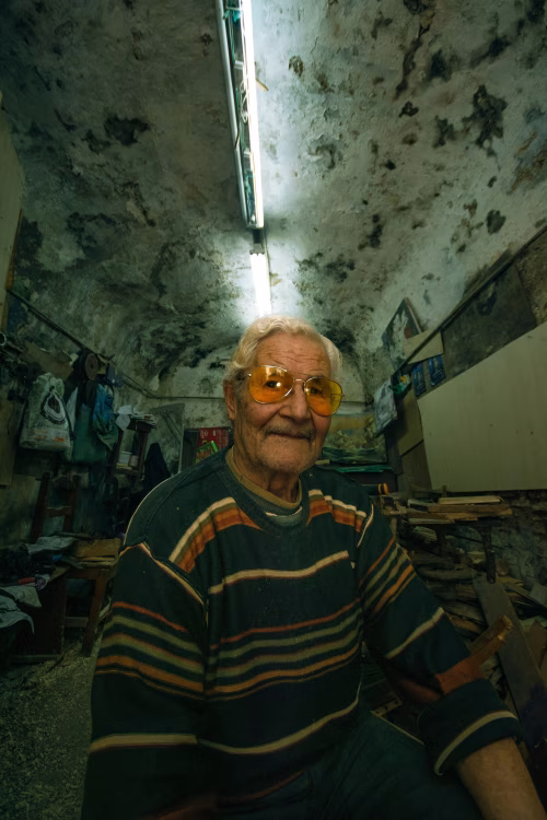 Elderly Man Sitting in a Rustic Workshop With Unique Lighting and Decor