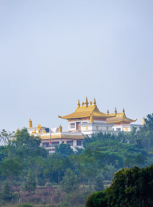 Golden Roof Temple Complex With White Walls Surrounded by Green Hills and Blue Sky