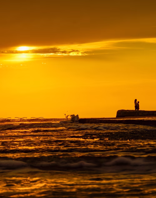 Golden Sunset Over Ocean With Silhouetted People Standing on Shoreline