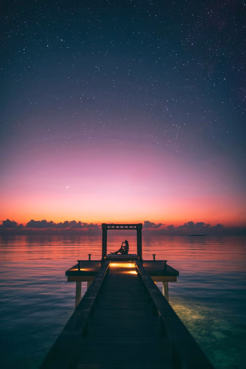 Idyllic Sunset Scene with Person Relaxing on a Pier Under Starlit Sky