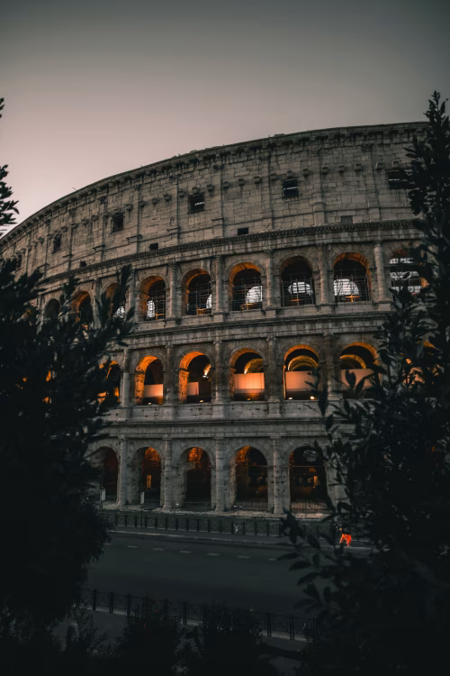 Illuminated Colosseum in Rome During Dusk Surrounded by Silhouetted Trees