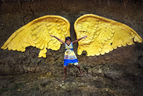 Joyful Child Standing Before Bright Yellow Wing Decoration on Rustic Wall