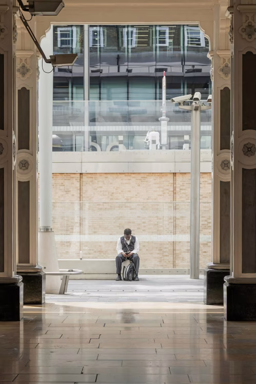 Man Sitting Alone in Modern Building Interior Using Smartphone