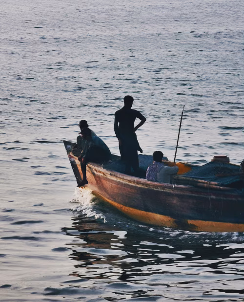 Men On A Small Fishing Boat Sailing Through Calm Water At Dusk