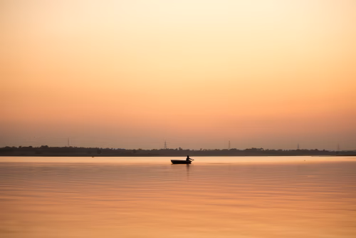 Silhouette Boat on Calm Sunset Lake With Soft Orange Sky and Tranquil Horizon at Dusk