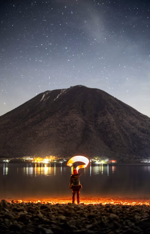 Silhouette of a Person Holding a Light in a Starry Mountain Scene
