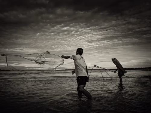 Silhouetted Fishermen Casting Net During Sunset Along Tranquil Riverscape