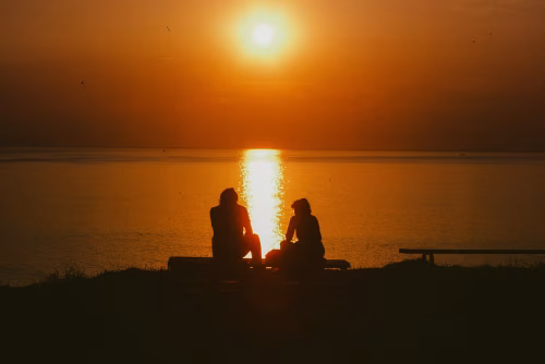 Silhouettes of Two People Sitting by a Sunset Over Calm Water