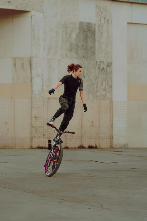 Skilled BMX Rider Performs Balance Trick On Street Near Industrial Concrete Wall