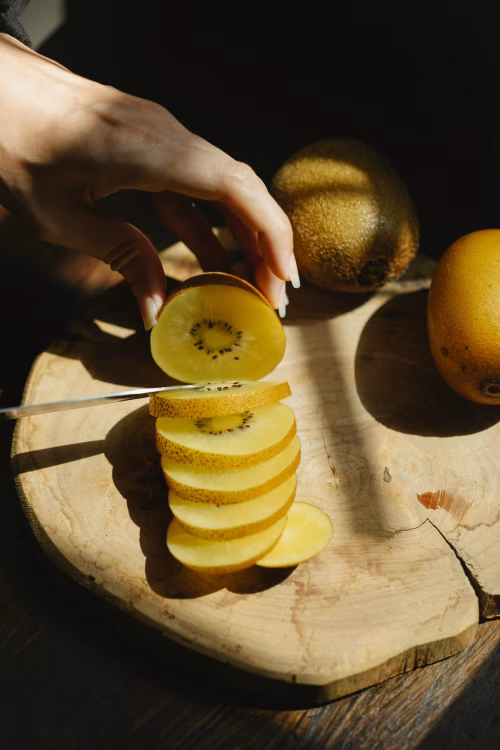 Sliced Yellow Kiwi on Wooden Board with a Hand Holding a Slice