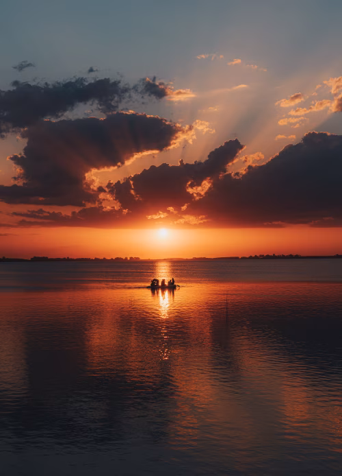 Sunset Rowboat With Silhouetted Figures Over Calm Water During Golden Hour Reflection