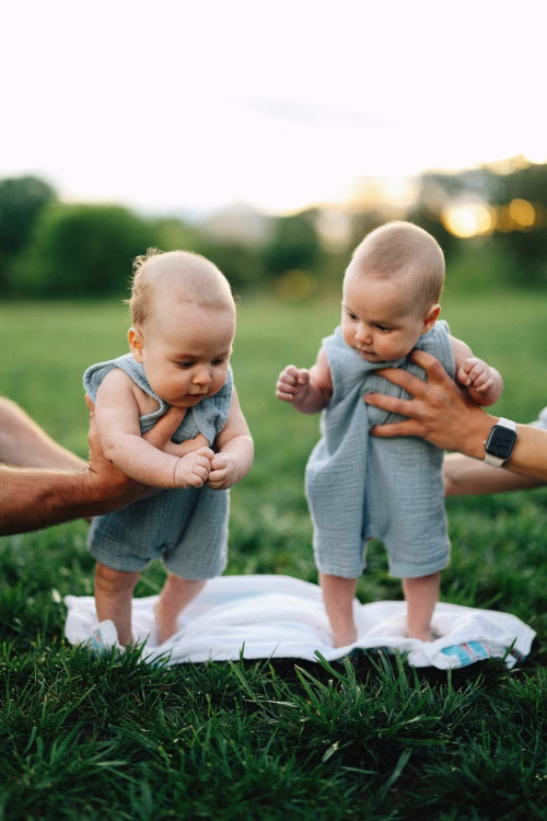 Two Babies in Matching Outfits Supported During Outdoor Playtime