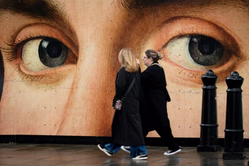Two Women Passing Large Artistic Eye Mural on City Street