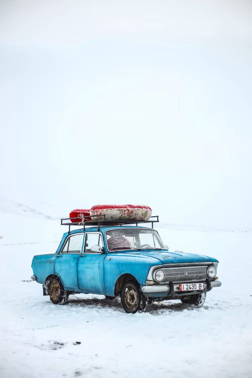 Vintage Blue Car on Snowy Landscape with Roof Cargo