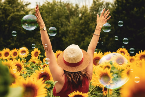 Woman Enjoying Summer Day in Sunflower Field With Colorful Bubbles