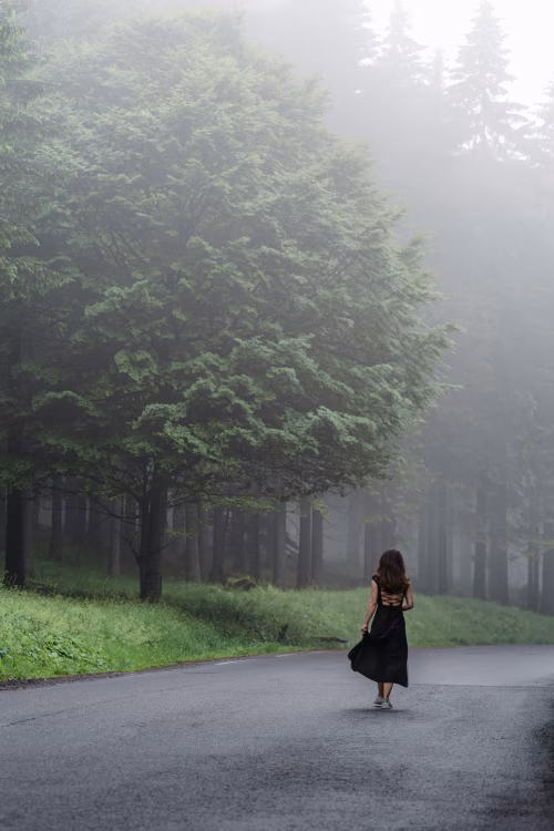 Woman Walking on a Foggy Road in a Forested Area